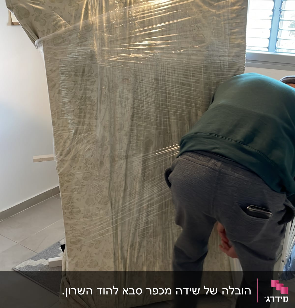 אדם עוטף מזרן בניילון שקוף בחדר